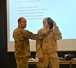 SSgt Clint Hazlett instructs on the proper wear of Mission Oriented Protective Posture (MOPP) gear at Joint Base San Antonio-Lackland, Texas on Feb. 5, 2024. Hazlett draws attention to the fastening structures and alignments below the chin to ensure greatest protection possible. (US Air Force photo by Alex Dieguez)