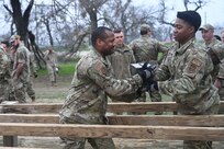 SSgt Kurtis Farmer passes a sand-filled ammunition container to Capt Cecil Calvin during a relay exercise at JBSA-Lackland, Texas on Feb. 9, 2024. The ‘six vaults’ obstacle is intended to be crossed using a series of high-steps without use of hands or significant delay in traversal. Participants are challenged during the final day by also alternating possession of the container which can weigh between 40 to 50 pounds. (US Air Force photo by Alex Dieguez)