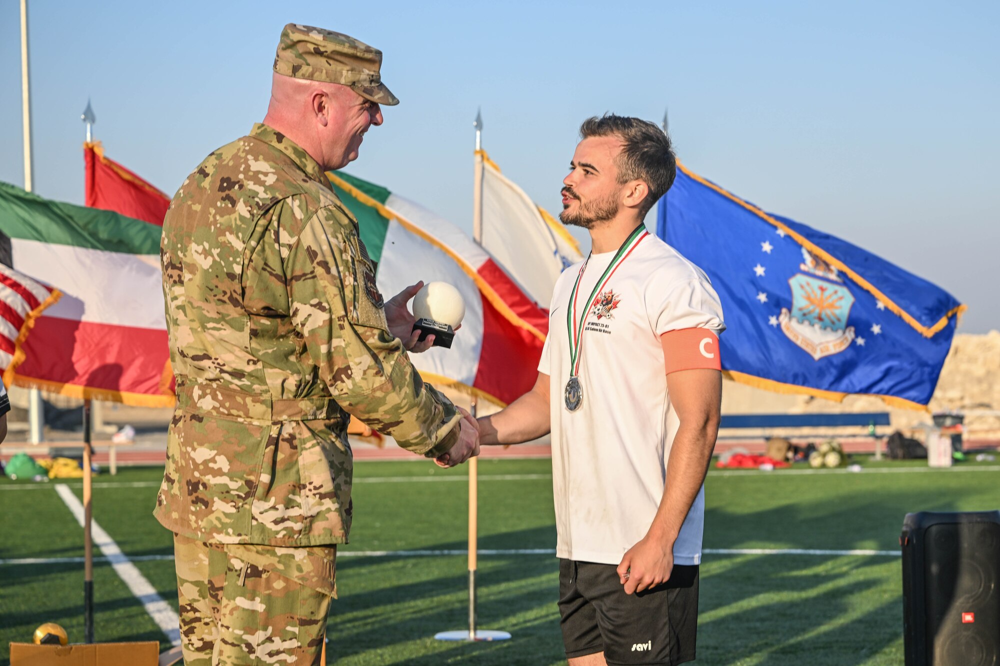 A man in uniform shakes a soccer player's hand.