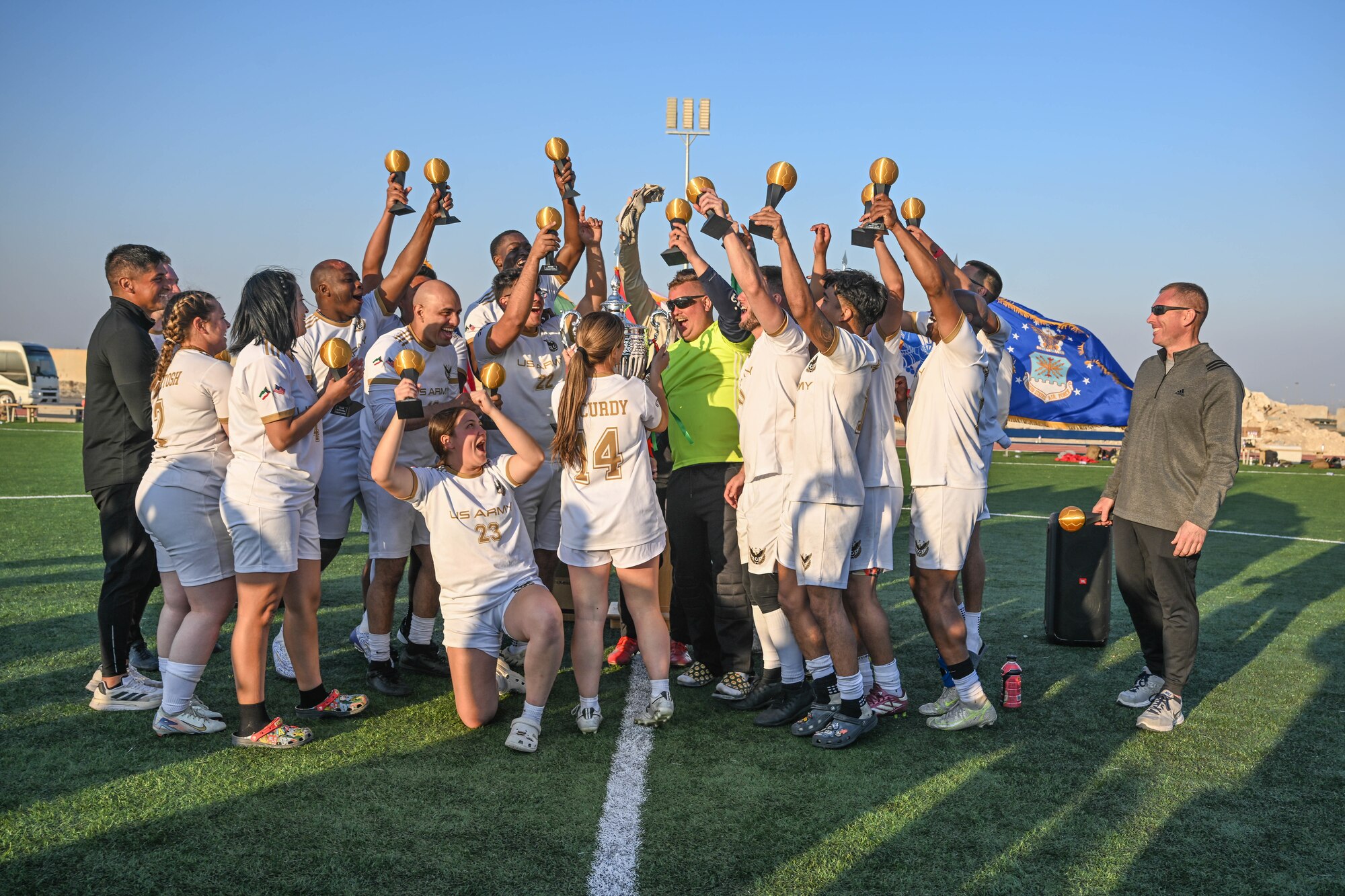 A group of people celebrate in soccer jerseys on a soccer field.