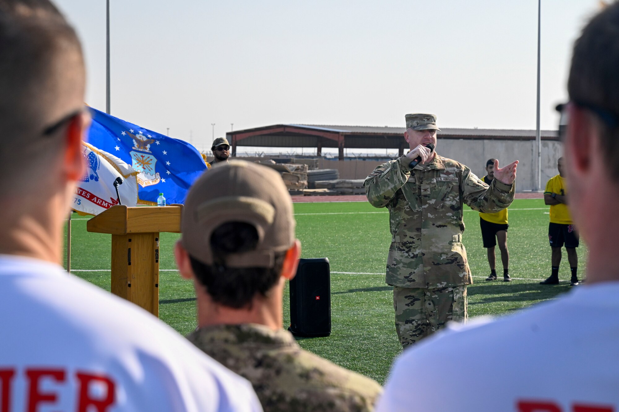 A man in uniform speaks into a microphone towards a crowd of people.