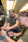 Civilian electronics integrated system mechanic explains F/A-18 Hornet circuit breaker panel repair to Marine.
