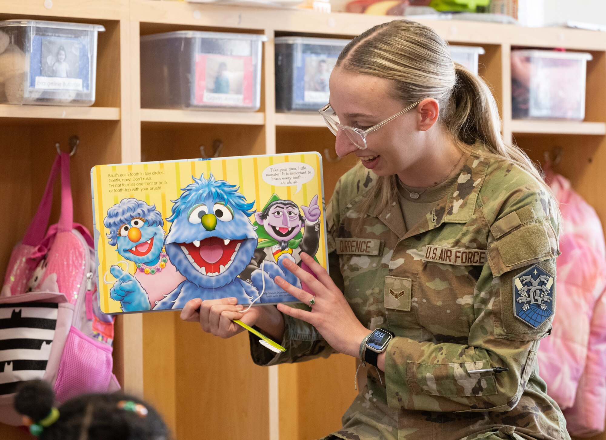 A member holds a children's book as she reads it to a group of kids.