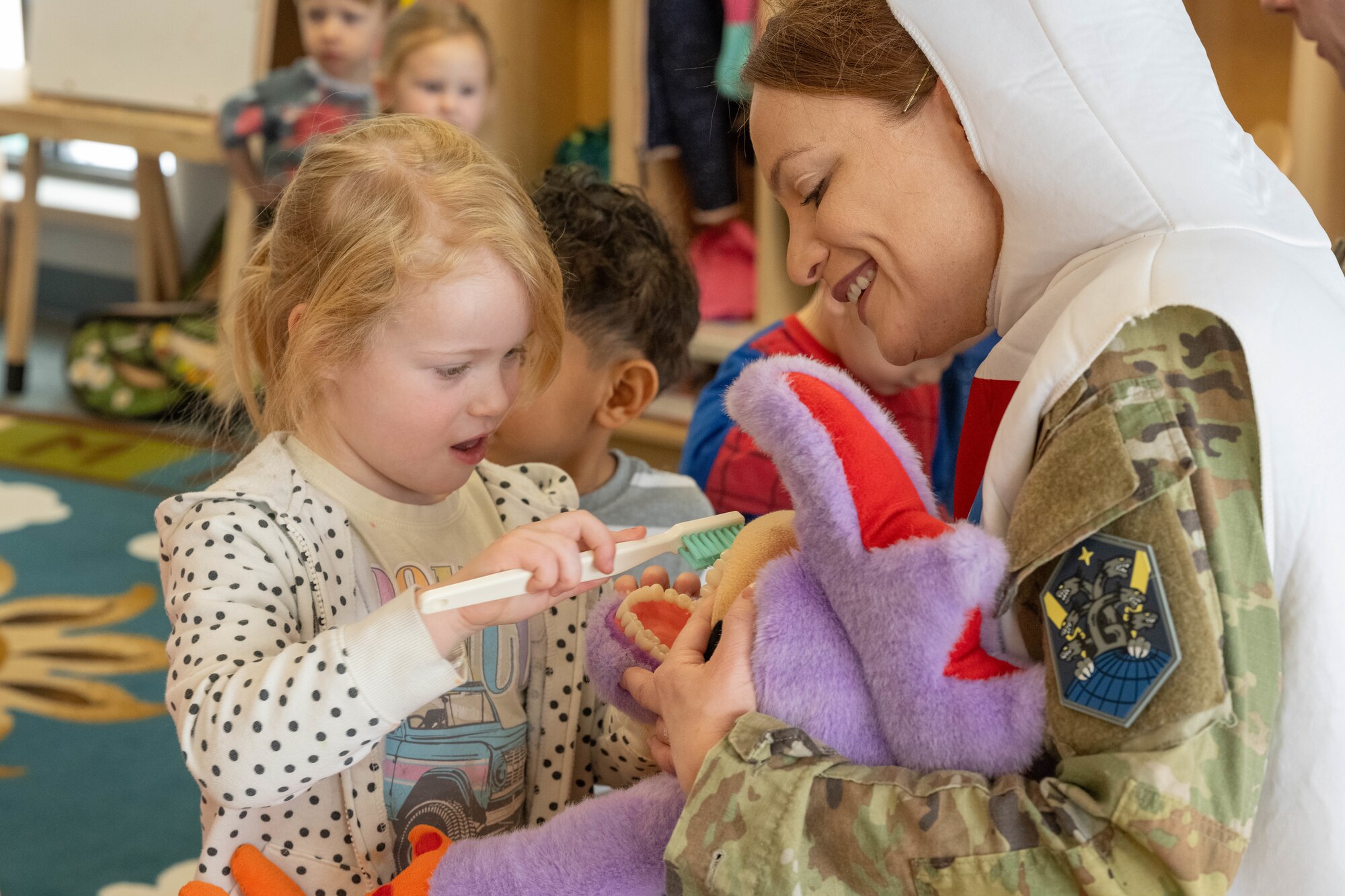 A child brushes the teeth of a stuffed animal as a member of the 21st Dental Squadron holds it.