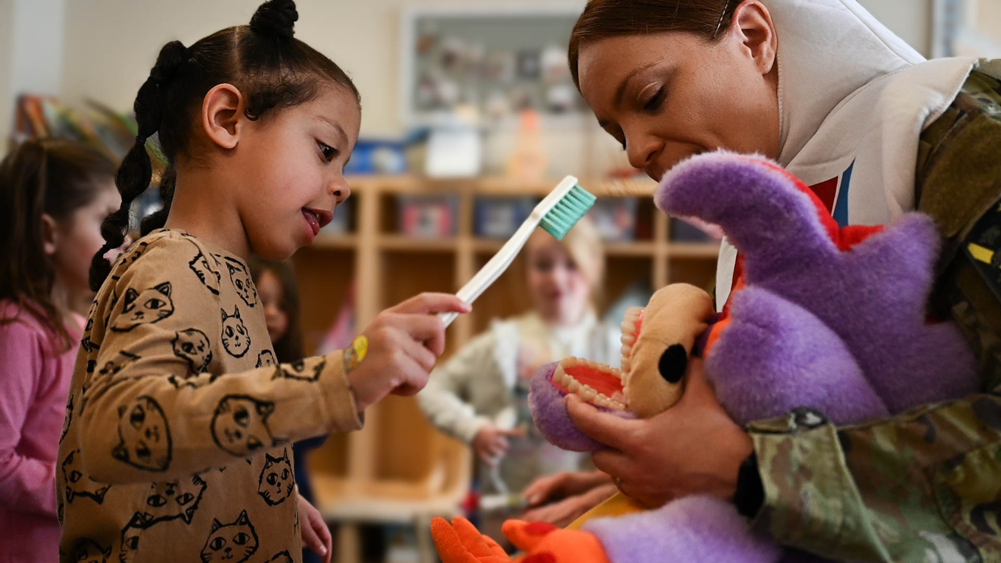 A child holds a toothbrush, as a member of the 21st Dental Squadron instructs her how to brush the stuffed animals teeth.