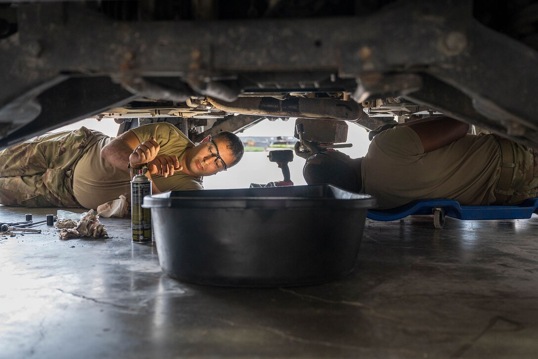 Two guardsmen work on maintenance underneath a vehicle.
