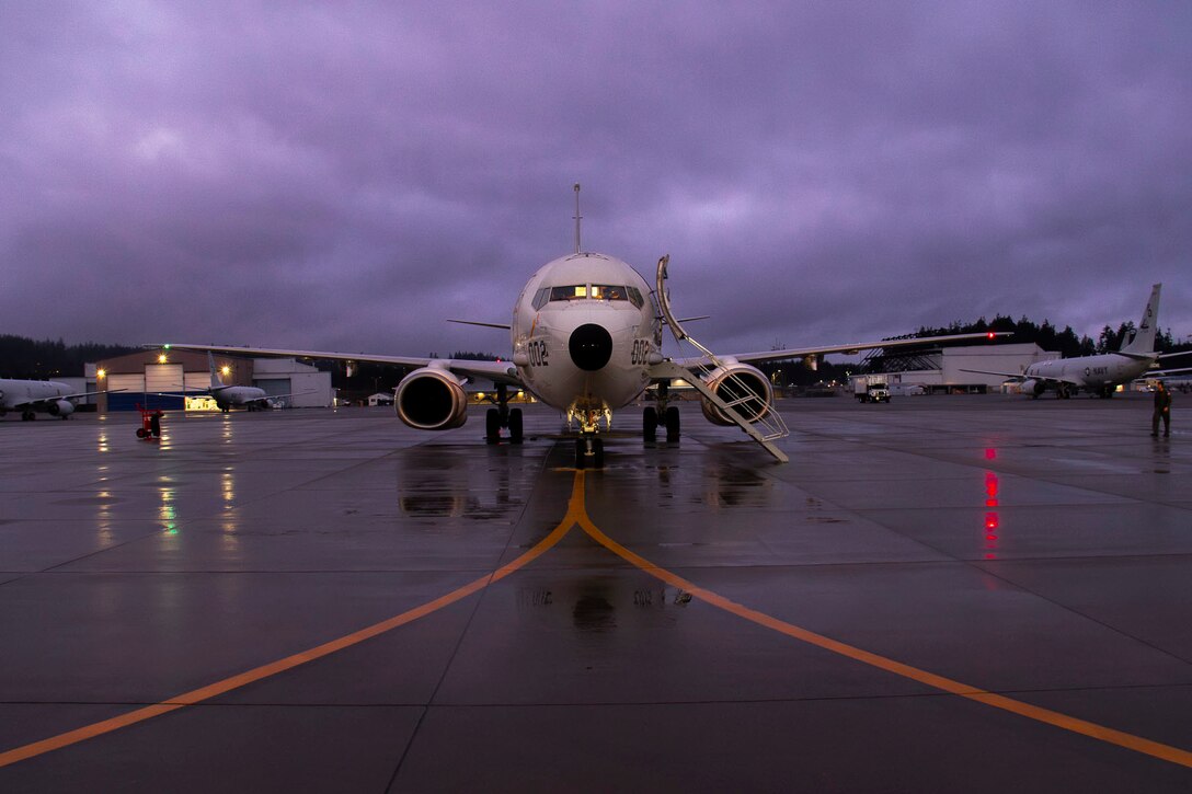 A P-8A Poseidon sits on the flight line at during a a cloudy, dark day.