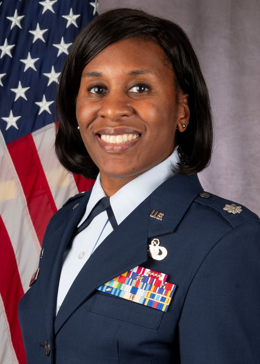 photo of a woman wearing a USAF uniform in front of a flag and gray bacgrkound