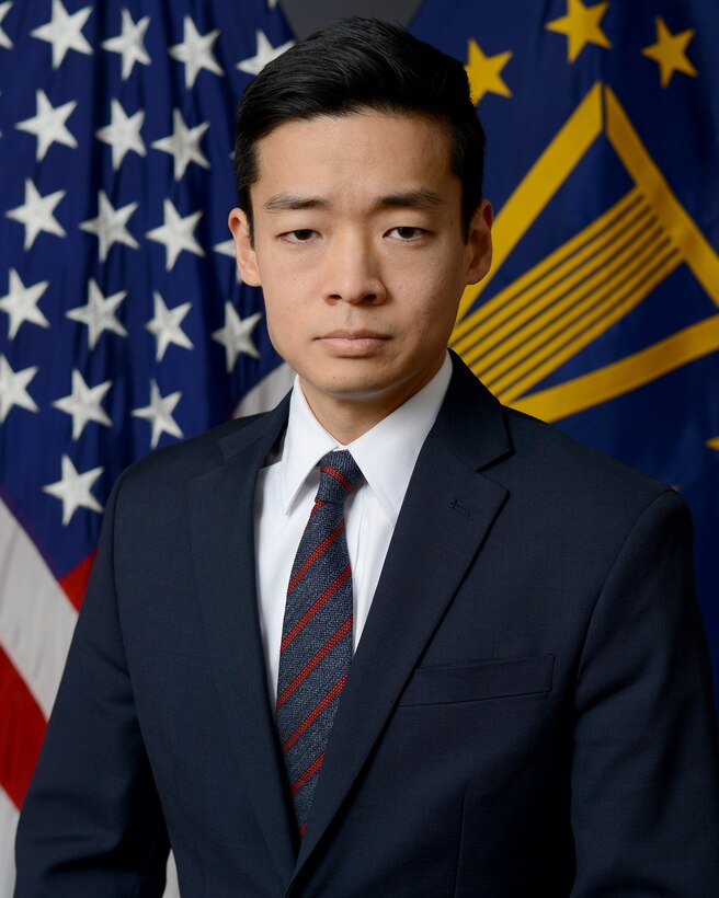 A man in a business suit sits in front of two flags.