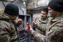 (From left to right) Airman 1st Class Erik Cruz, Staff Sgt. Micheal Villarreal and Master Sgt. Matthew Yordt, all heating, ventilation, air conditioning and refrigeration specialists assigned to the 5th Civil Engineer Squadron, use a voltmeter on an air switch to troubleshoot a furnace at Minot Air Force Base, North Dakota, Feb. 19, 2025. At locations like Minot AFB, where the winters can reach dangerously low temperatures, HVAC/R military and civilian engineers sustain critical heating systems. (U.S. Air Force photo by Senior Airman Kendra A. Ransum)