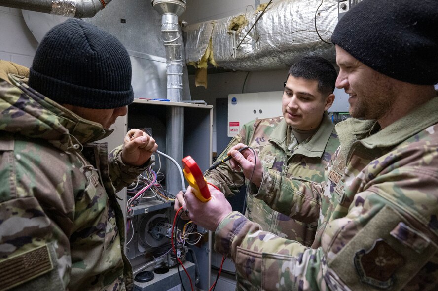 (From left to right) Airman 1st Class Erik Cruz, Staff Sgt. Micheal Villarreal and Master Sgt. Matthew Yordt, all heating, ventilation, air conditioning and refrigeration specialists assigned to the 5th Civil Engineer Squadron, use a voltmeter on an air switch to troubleshoot a furnace at Minot Air Force Base, North Dakota, Feb. 19, 2025. At locations like Minot AFB, where the winters can reach dangerously low temperatures, HVAC/R military and civilian engineers sustain critical heating systems. (U.S. Air Force photo by Senior Airman Kendra A. Ransum)