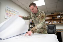 U.S. Air Force Capt. Dylan Bechen, the operations flight commander assigned to the 5th Civil Engineer Squadron, looks at a base map in his office on Minot Air Force Base, North Dakota, Feb. 19, 2025. The 5th CES’ heating, ventilation, air conditioning and refrigeration specialists provide around-the-clock emergency response and preventative maintenance for 573 facilities for Team Minot. (U.S. Air Force photo by Senior Airman Kendra A. Ransum)