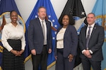 Four people pose for a picture after coin presentation.