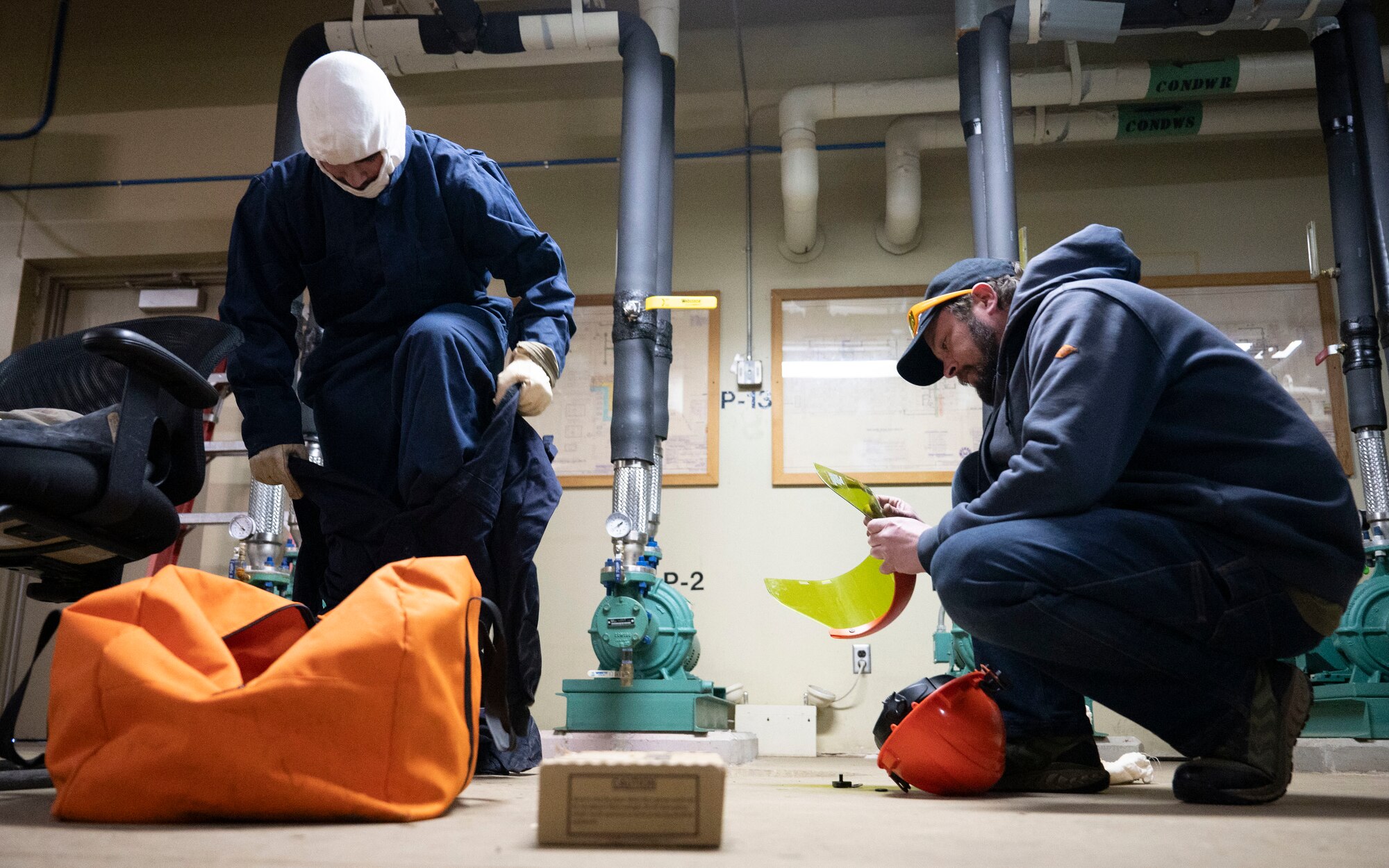 Senior Airman Payton Jones, a 5th Civil Engineer Squadron heating, ventilation, air conditioning and refrigeration specialist, puts on an Arc Flash suit while Aaron Puuri, an HVAC maintenance mechanic, prepares the suit’s face mask at the Flight Simulation Training building on Minot Air Force Base, North Dakota, Feb. 19, 2025. The suit is personal protective equipment against possible arc flashes when working on electrical panels. (U.S. Air Force photo by Senior Airman Kendra A. Ransum)