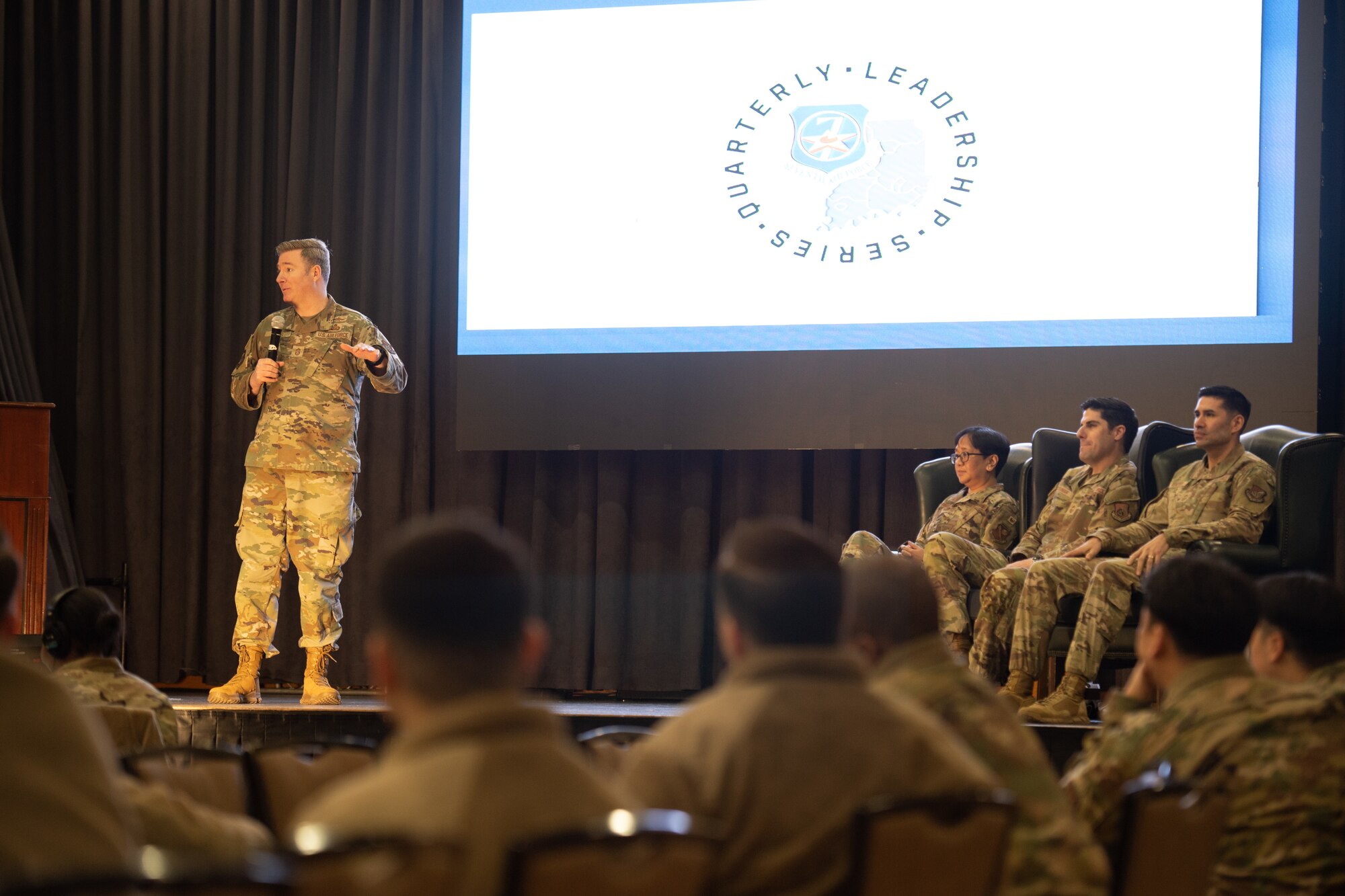 Military members are on stage. Slides are projected in the background that say Quarterly Leadership Series.