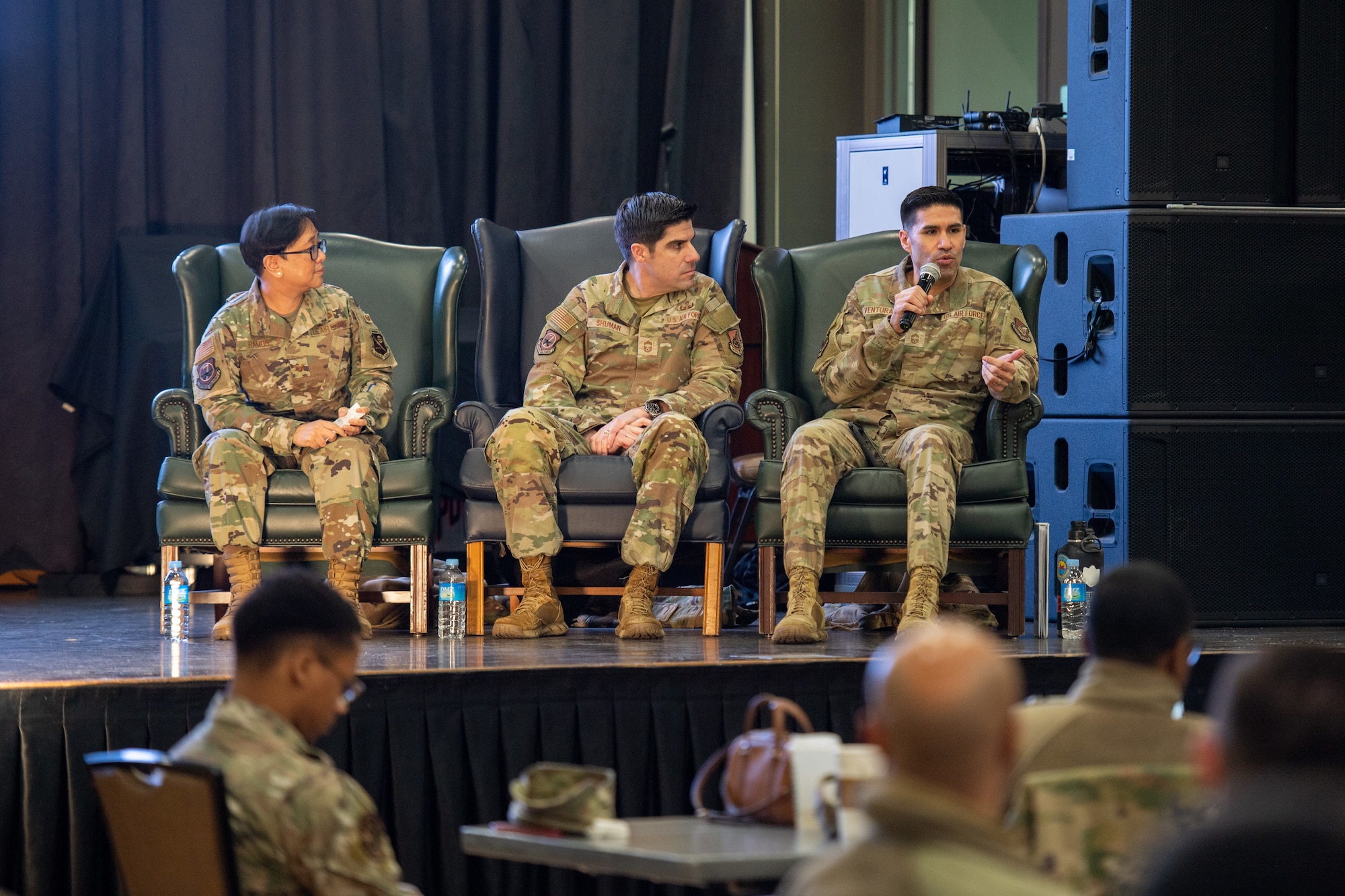 Three military members are on stage, military members are in the audience.