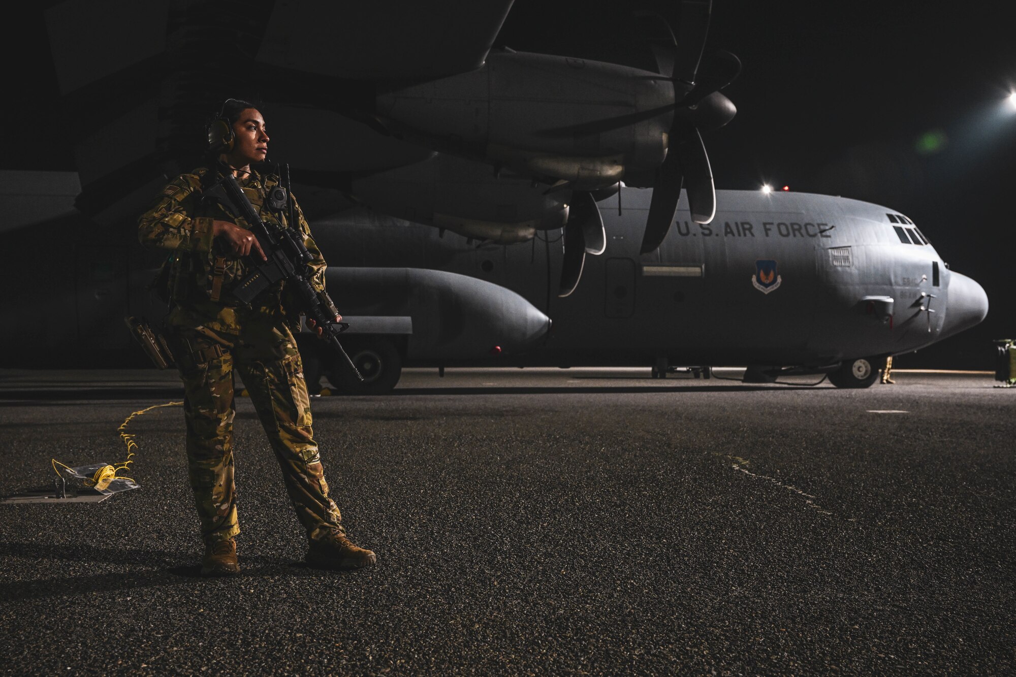 A woman in uniform stands next to a plane holding a rifle.