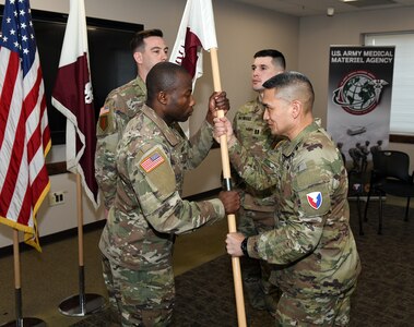 Col. Joselito “Joe” Lim, commander of the U.S. Army Medical Materiel Agency, passes the colors to Capt. Paul Abucher, signifying his trust in him to lead as USAMMA’s new Headquarters and Headquarters Detachment commander during a change of command ceremony Feb. 21 at Fort Detrick, Maryland. The ceremony also recognized outgoing commander Capt. Andrew Whittenbarger.