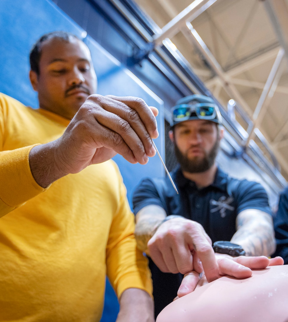 An instructor shows a SurgeMain Sailor the procedure for inserting a large-bore needle for the purpose of decompressing a simulated tension pneumothorax Feb. 2, during Tactical Combat Casualty Care training on Naval Base Kitsap-Bremerton, Washington. (U.S. Navy photo by MC1 Jeffrey J. Hanshaw)