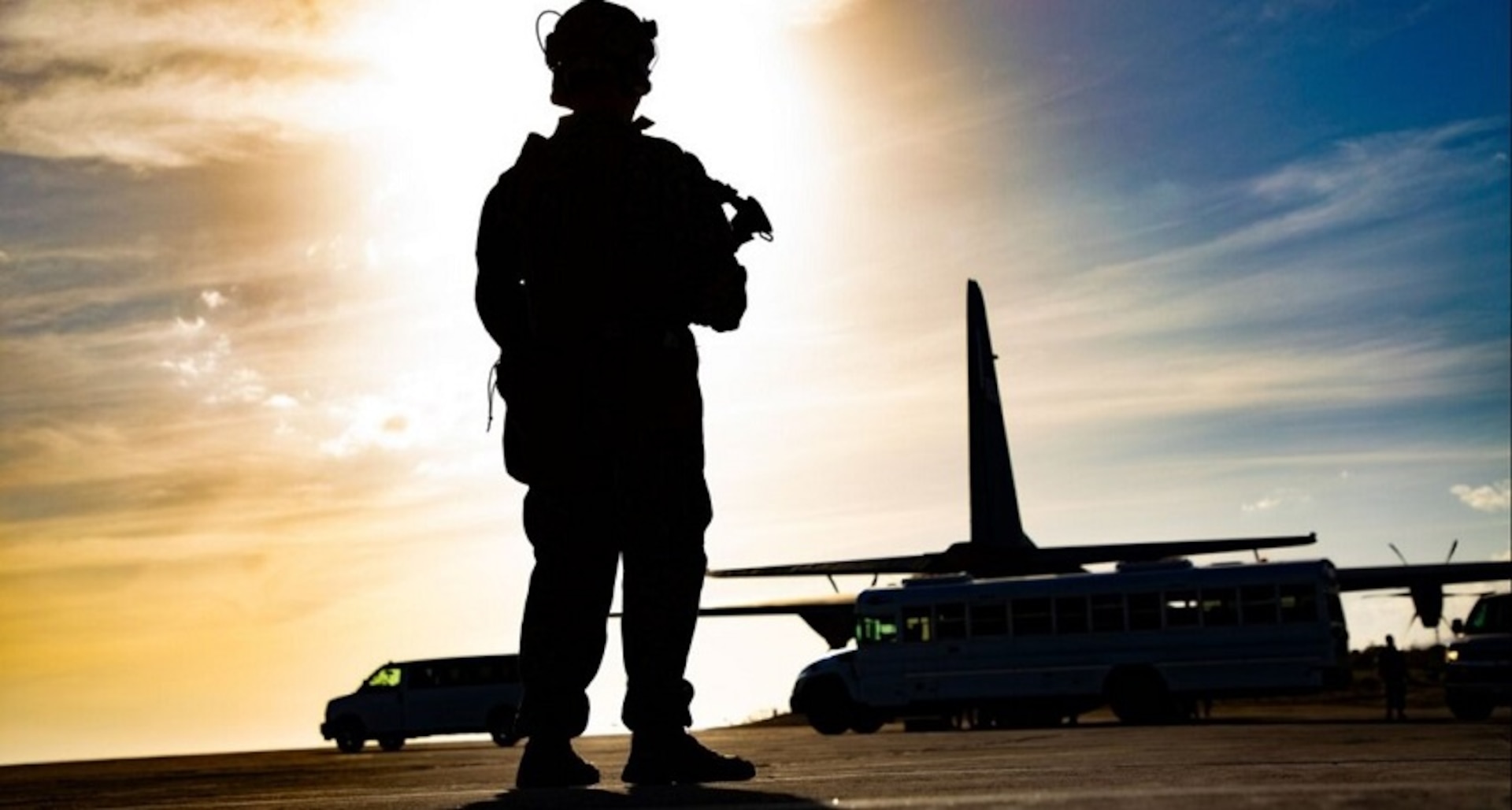 A silhouetted soldier stands on an airfield with an aircraft in the background.