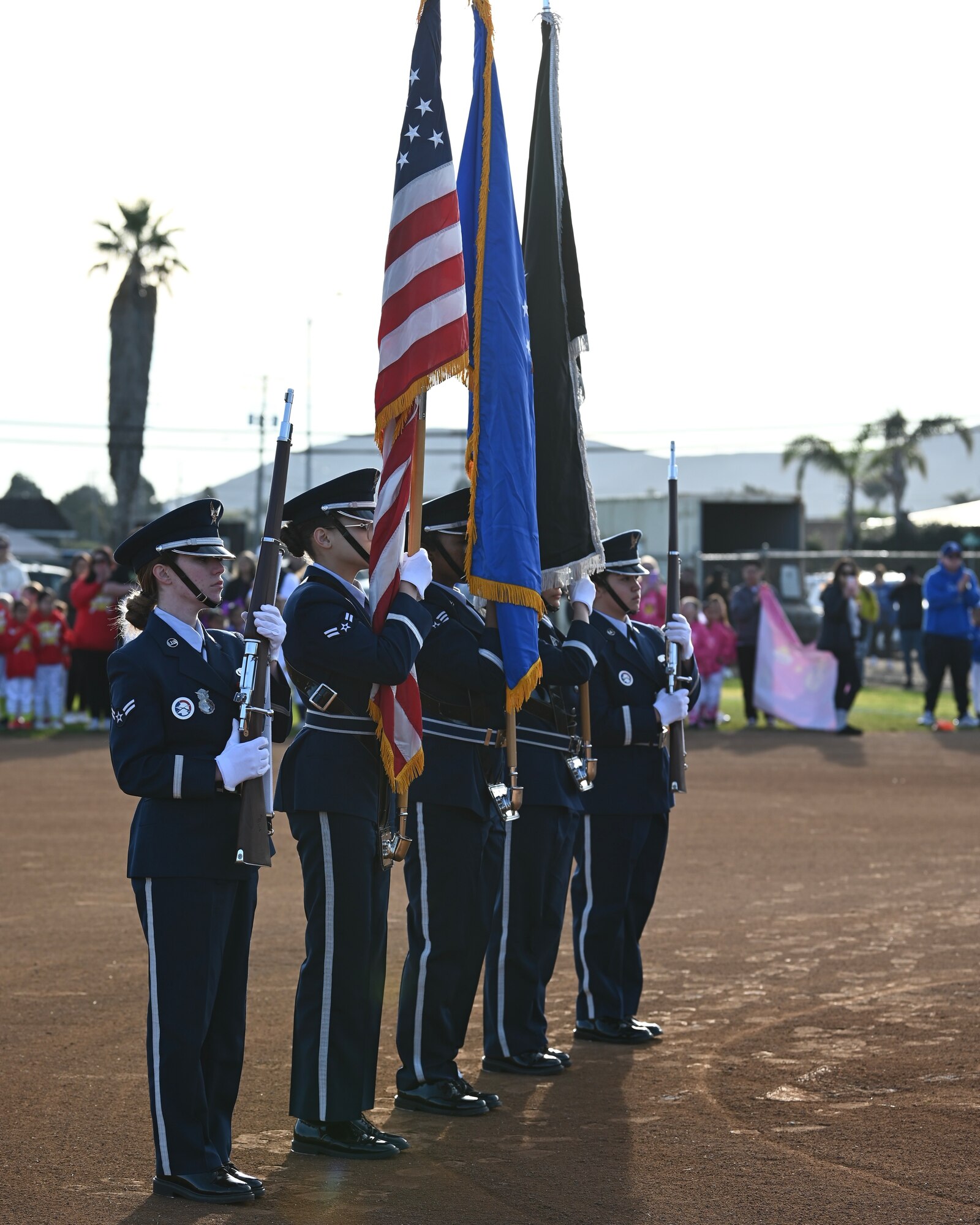 military honor guard holds flags and guns during the posting of the colors on a softball field, kids in the background