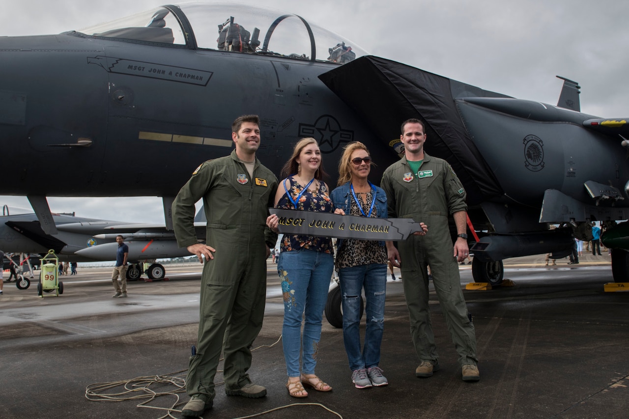 Four people pose for a photo in front of a fighter jet.