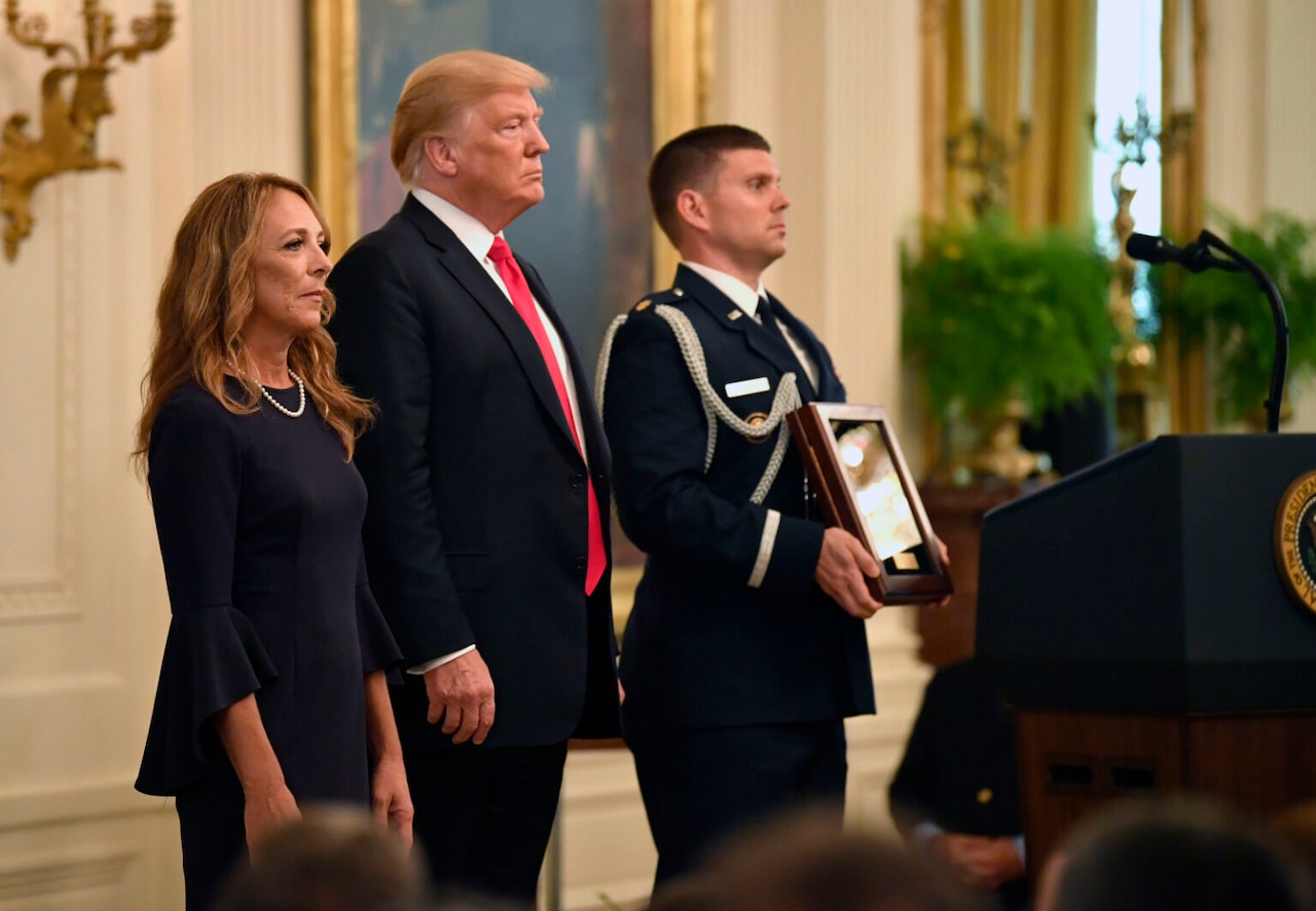 Three people near a podium stand looking forward. One holds a plaque.