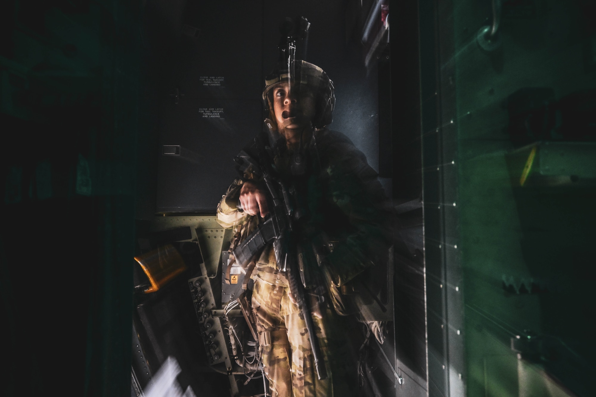 A woman in uniform stands in the doorway of a plane holding a rifle.