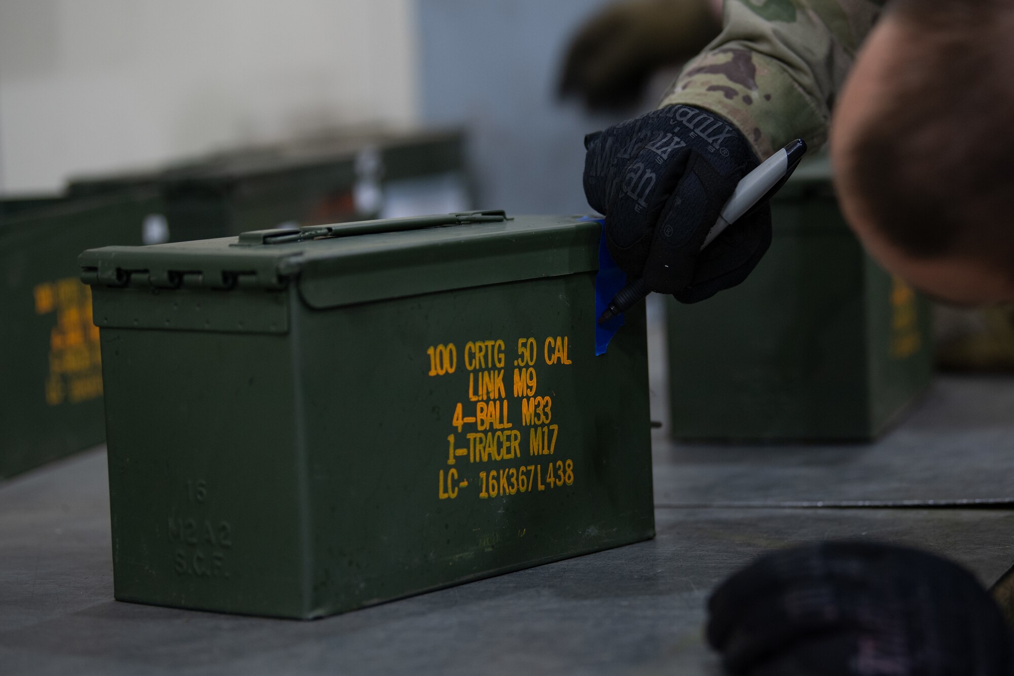 An Airman writes on the side of a green ammo box.