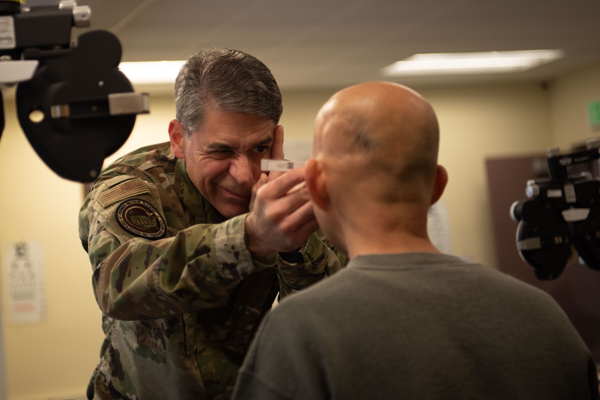 A uniformed optometrist exams a civilian patient's eyes.