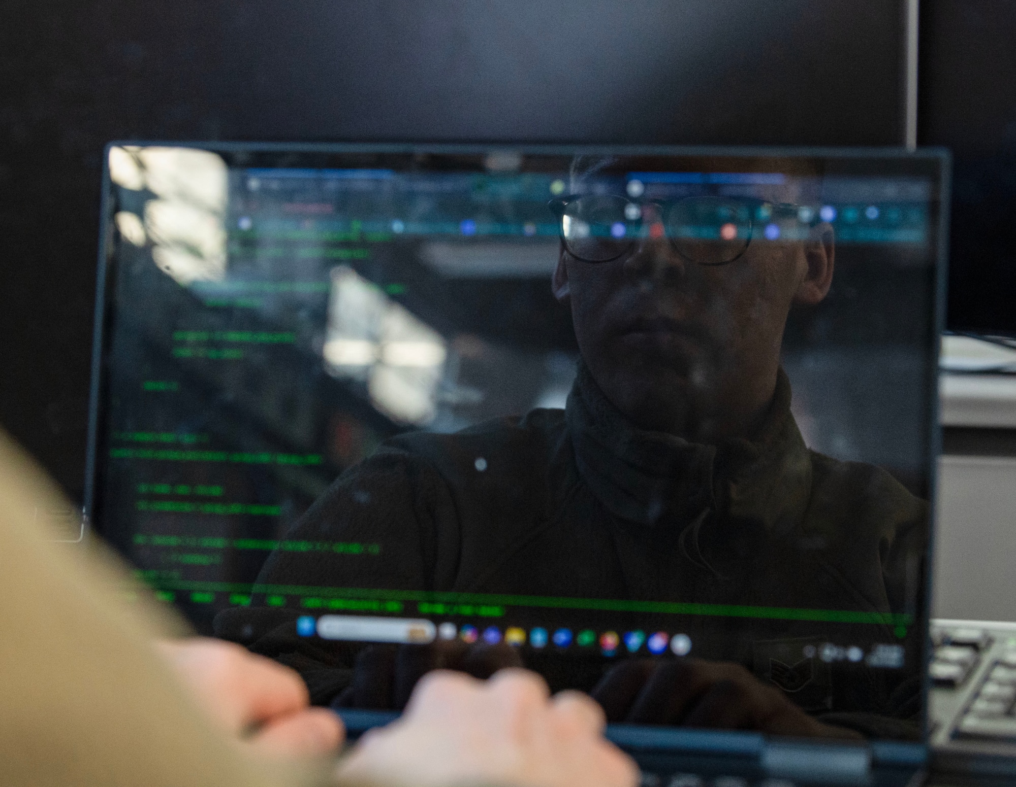 A laptop screen reflects the face of an Airmen working on it.