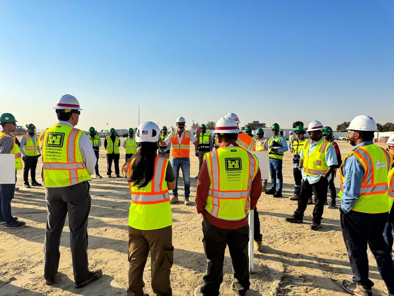 A group of people in helmets and safety vests listen to a safety briefing.