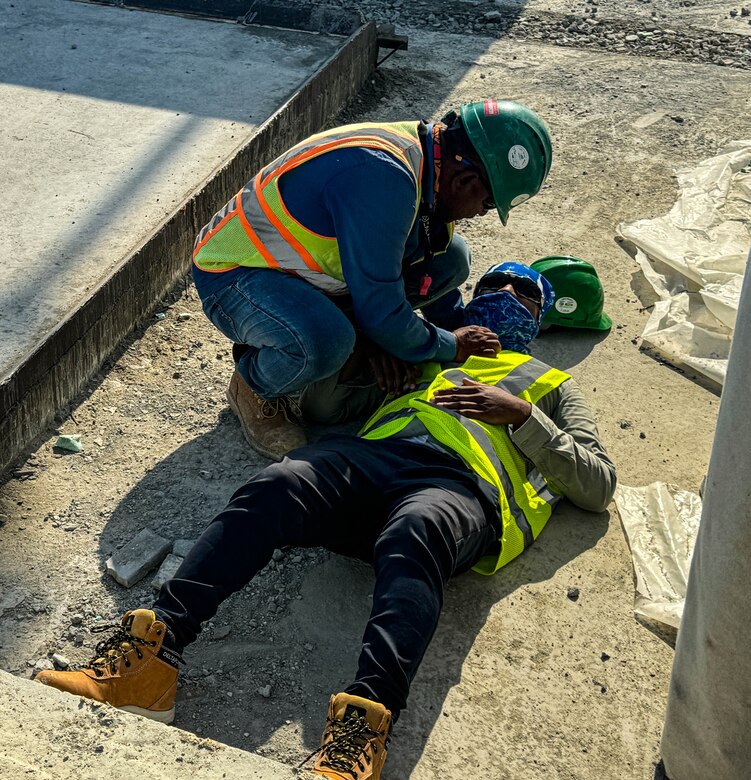 Man in distress laying on ground while another man assists during a safety drill.