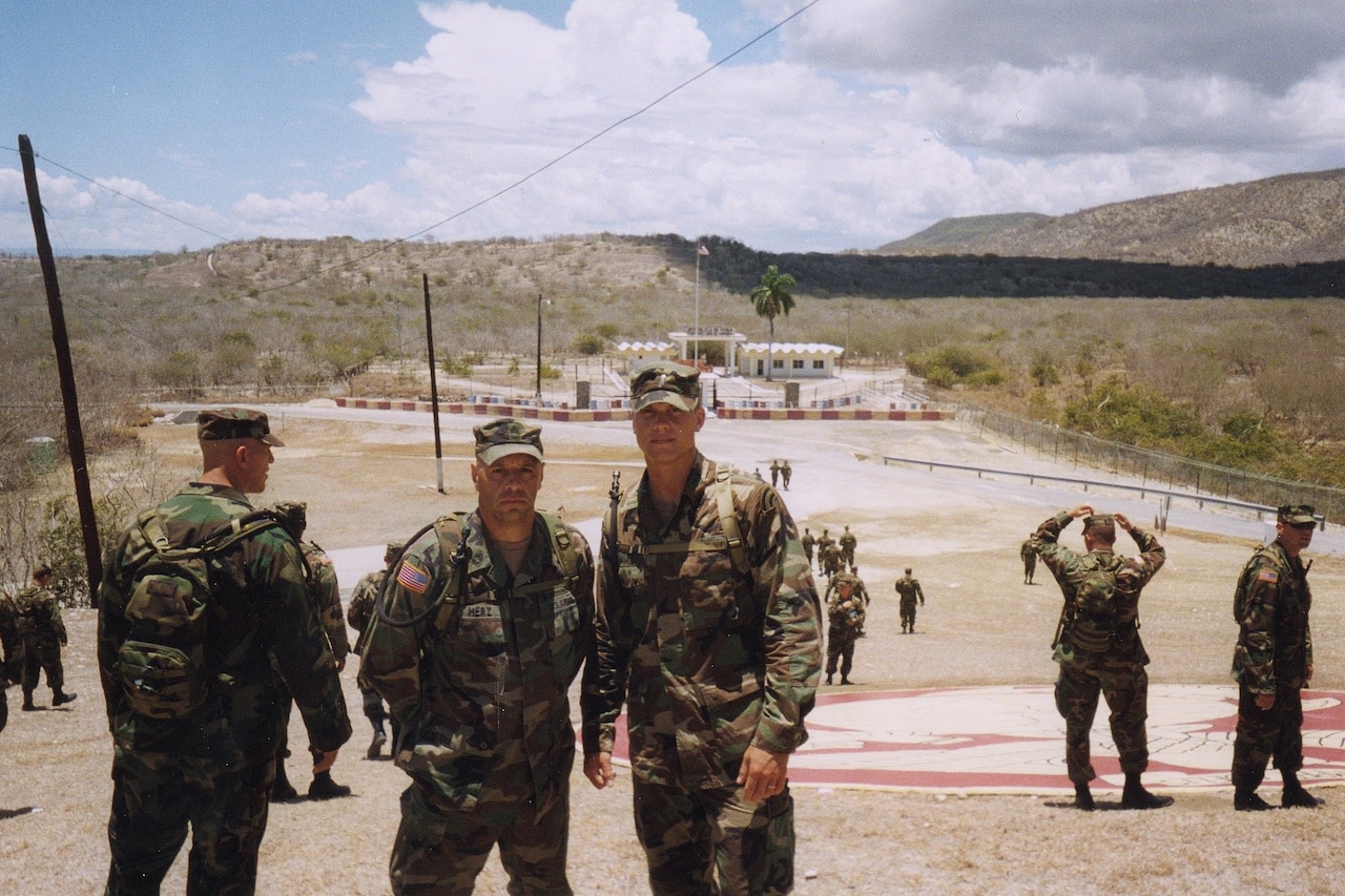 Two men in camouflage uniforms are standing outside posing for the camera.