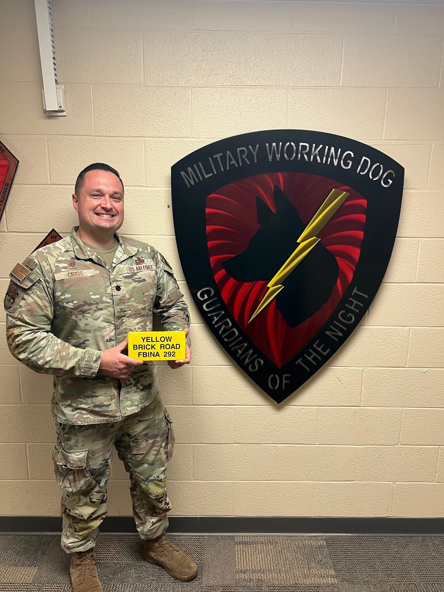 Air Force Lt. Col. stands with a yellow brick in front of the Military Working Dogs shield.