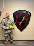 Air Force Lt. Col. stands with a yellow brick in front of the Military Working Dogs shield.