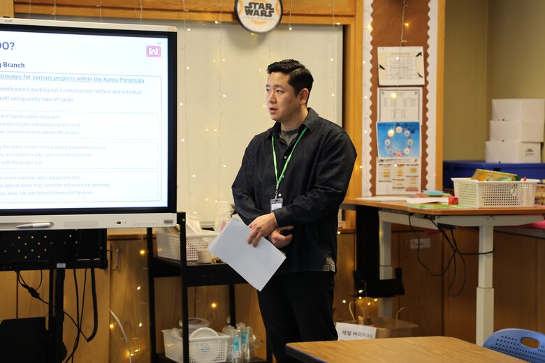 Seung Ho Lee, cost engineer, U.S. Army Corps of Engineers – Far East District, explains the role of cost engineering in construction during a presentation at Humphreys High School, Camp Humphreys, on Feb. 21, 2025. Using a slide outlining cost estimates for various projects across the Korean Peninsula, Lee discussed key factors such as material, labor, and indirect costs, providing students with insights into the financial planning behind military construction. (U.S. Army photo by Yohan An)