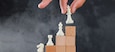 Business success concept with chessboard on wooden and foggy background side view. man placing figure on pyramid of blocks.