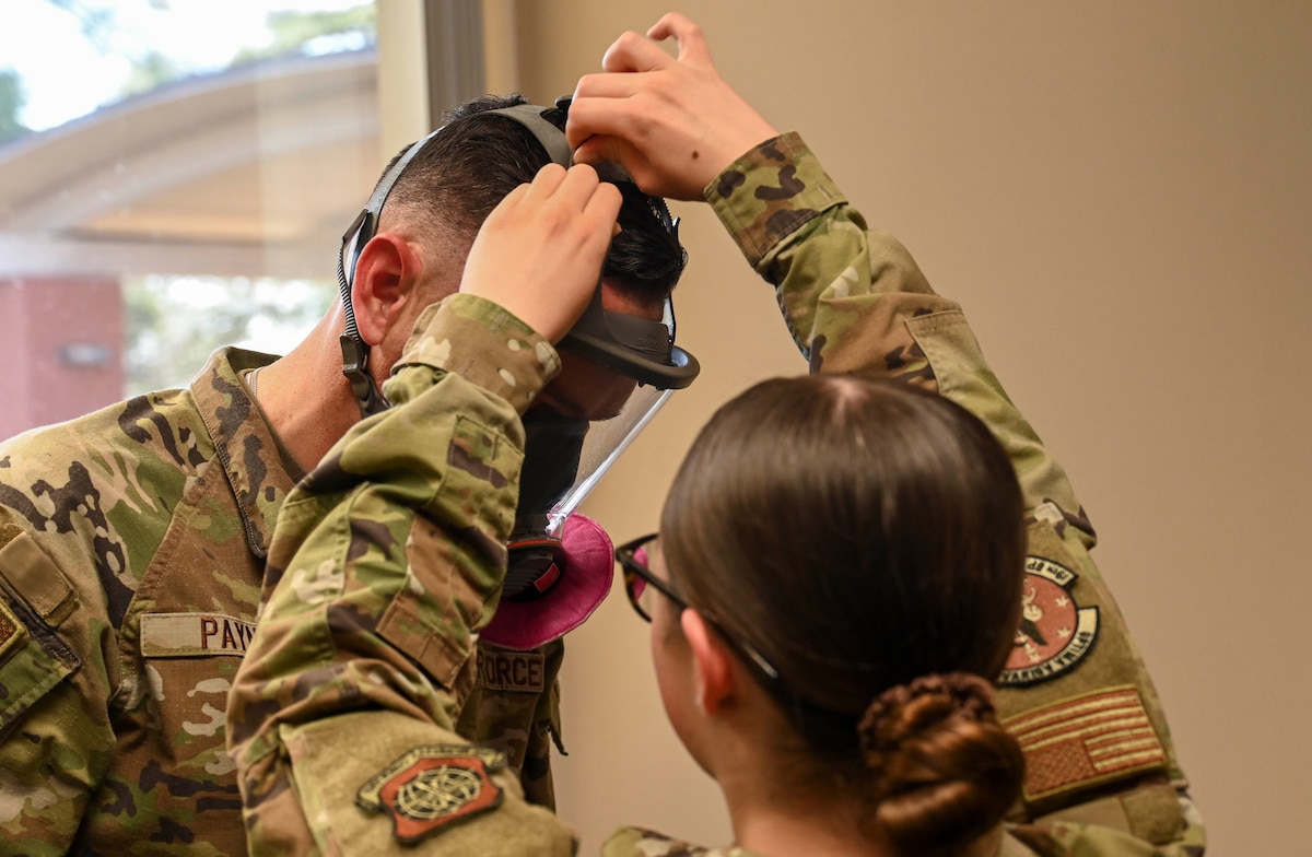 An airman adjusts straps on a mask for another Airmen