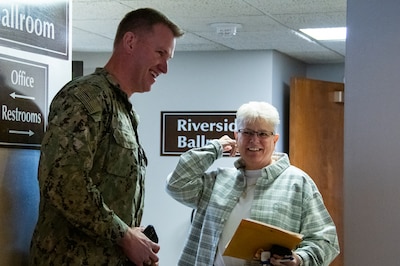 A man in a camouflage military uniform smiles at a woman in a hallway.
