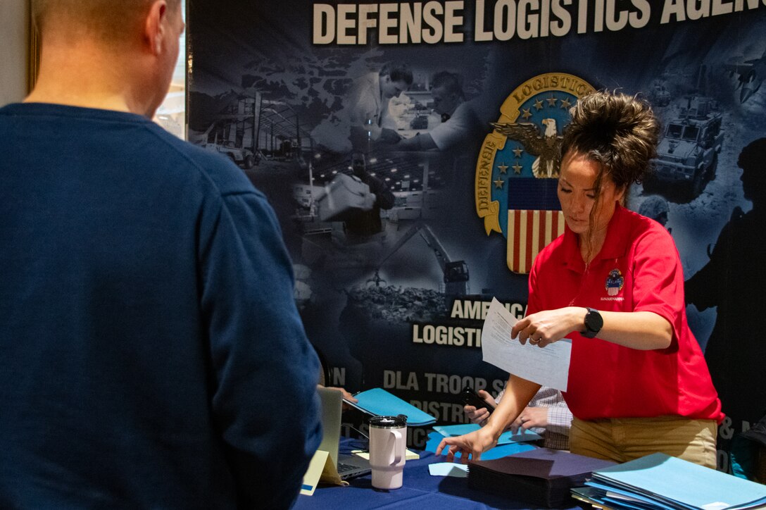 A woman in a red shirt stands at an information booth looking at a sheet of paper.