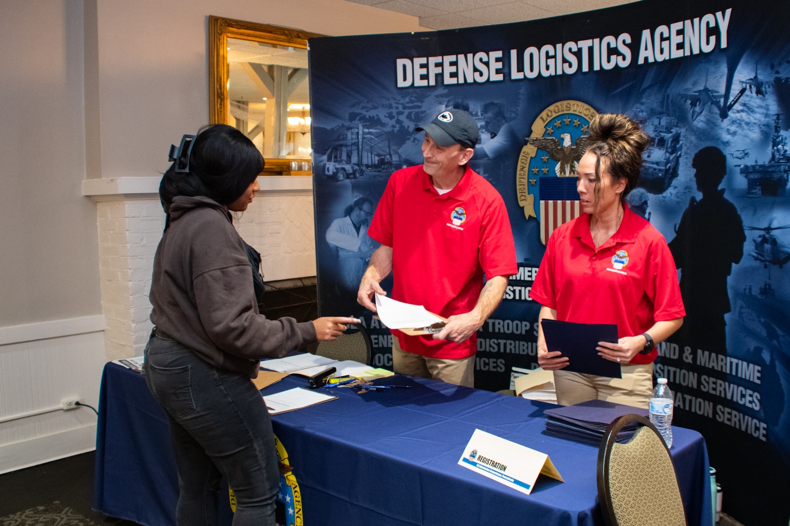 A person talks to two other people standing behind a table at an information booth.