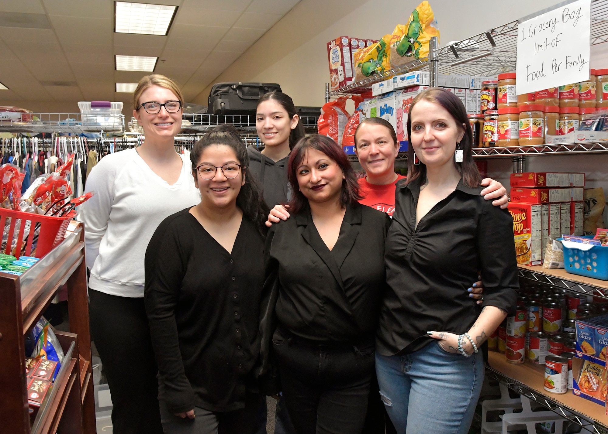 Volunteers stand next to shelves filled with packaged food items.