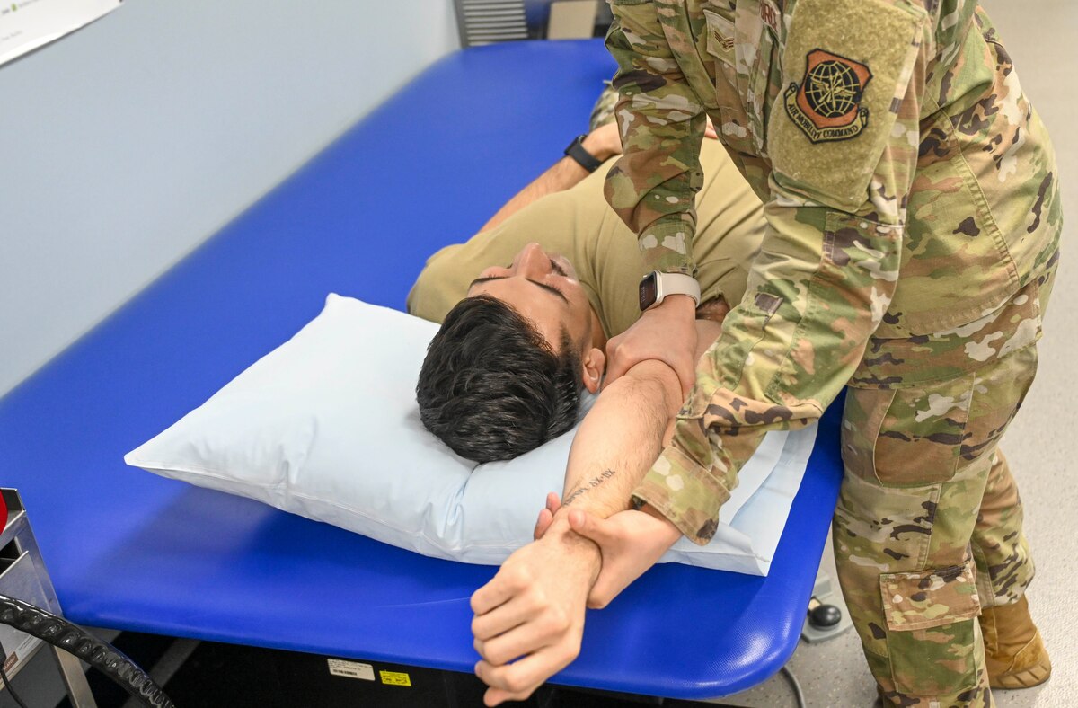 An Airmen helps a patient complete an arm stretch