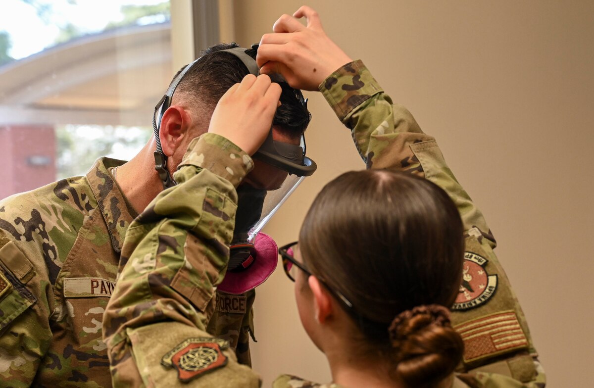 An airman adjusts straps on a mask for another Airmen