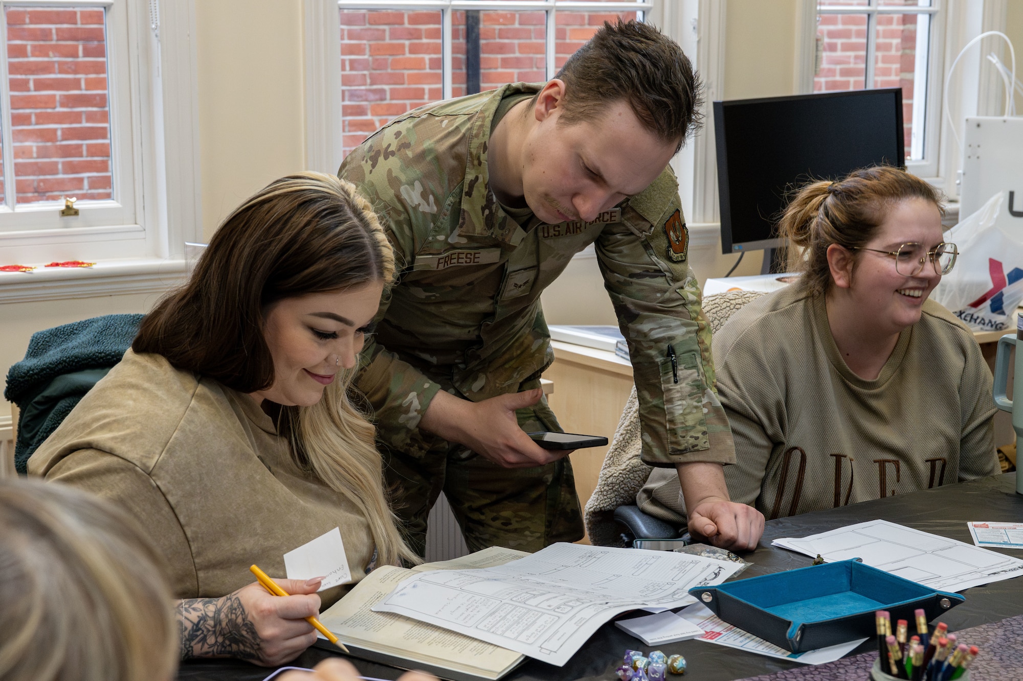 U.S. Air Force Airman 1st Class Grant Freese, center, 48th Component Maintenance Squadron environmental and electrical aircraft maintainer, looks over a character sheet for Danielle Brome, 100th Force Support Squadron library technician, at RAF Mildenhall, England, Feb. 26, 2025.