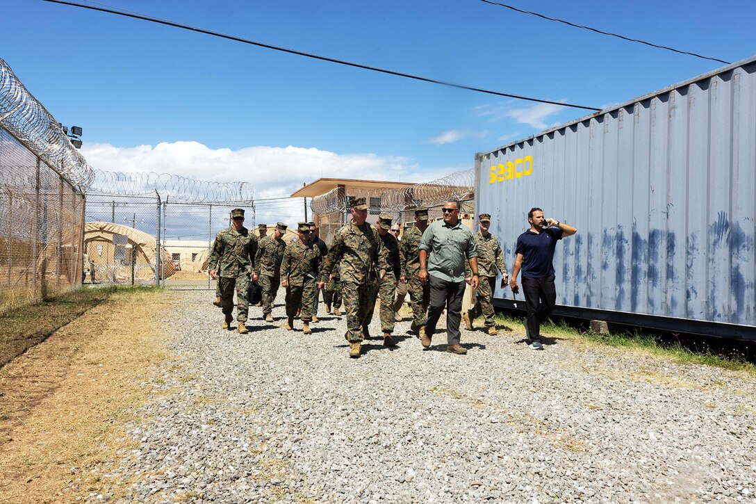 A commander speaks to a person a fellow service members walk behind them on a rocky surface.