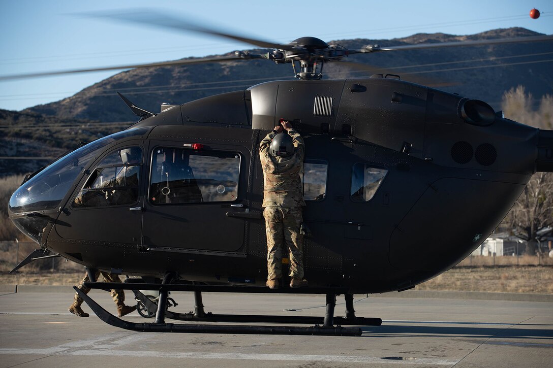 A soldier works on a helicopter in front of a mountain.