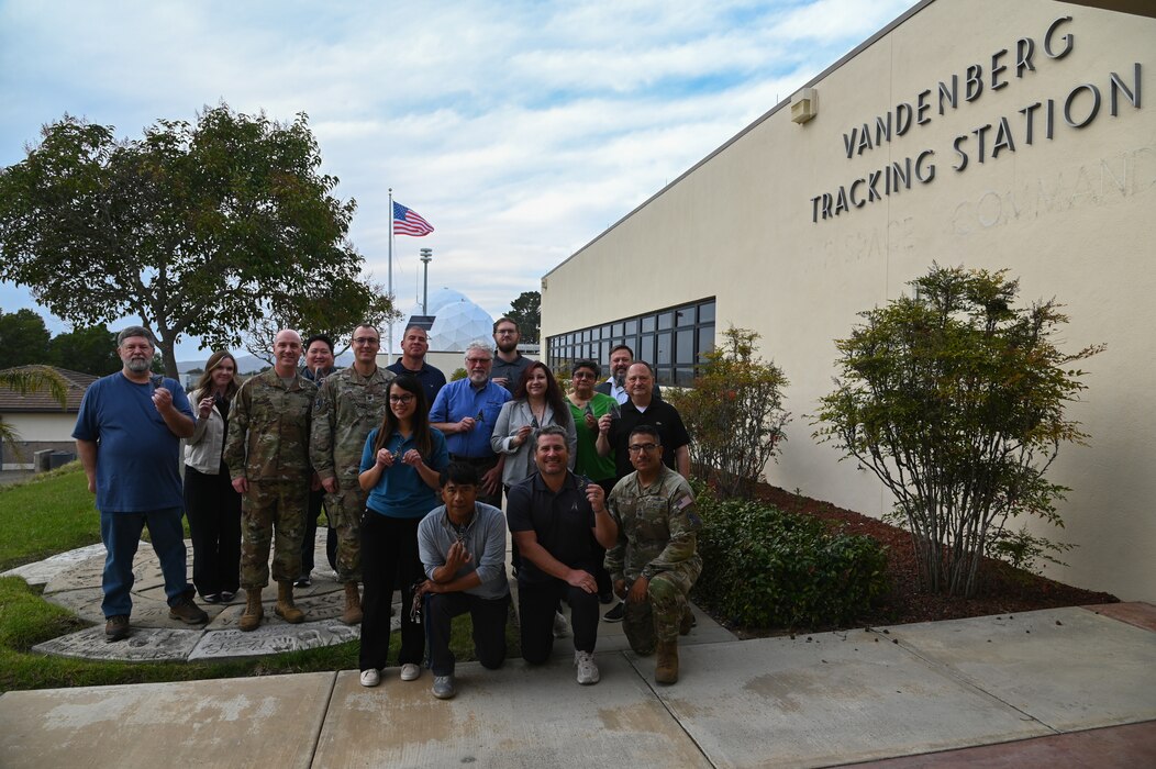 21 sops and md 31 members pose with thew ne md 312 patch outside of vandenberg tracking station, sign to the right and weather balls behind them with us flag