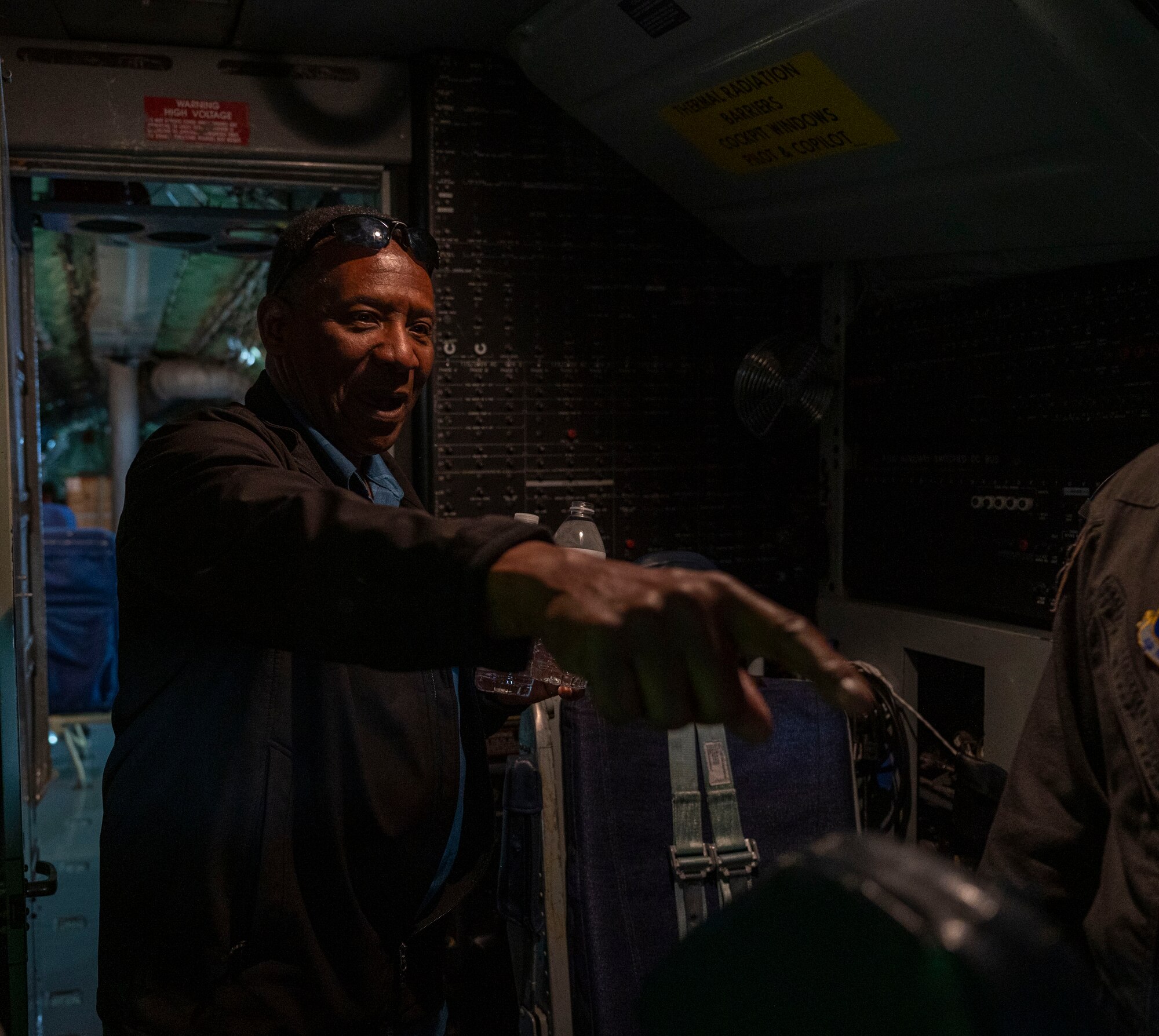 Rev. Ducarmel Cyrius is touring the inside of a KC-135 air craft. The image depicts Cyrius pointing towards a button and asking a question.